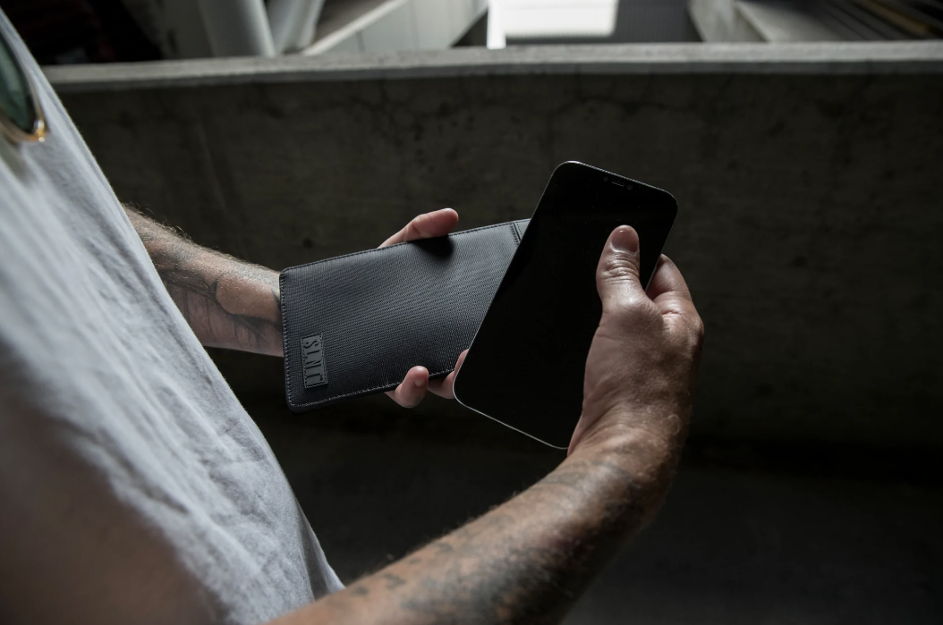 Person holding a smartphone and a black Faraday Phone Sleeve with a blurred background