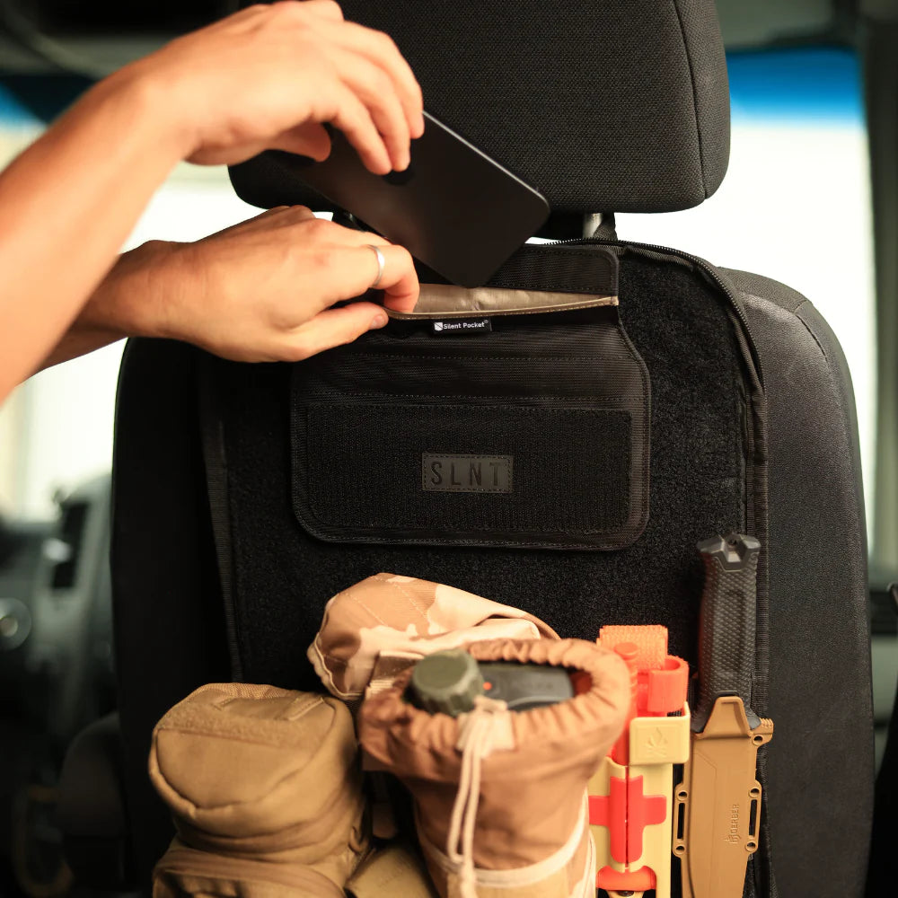 Person adjusting a black Velcro Faraday  case on a car seat with tactical gear underneath