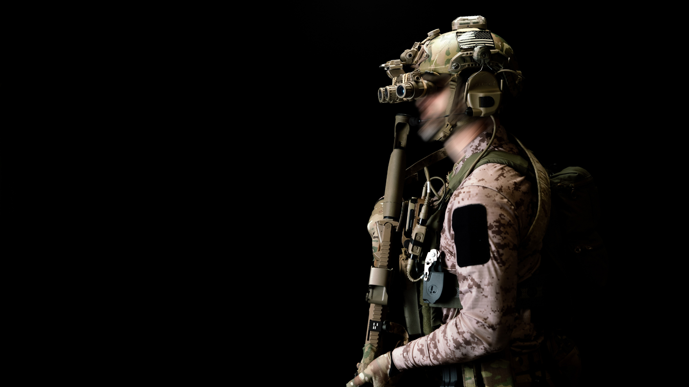 A soldier carrying an assault riffle facing to the floor. His face is blurred and he wears a helmet, 13th heaven top and night vision goggles.