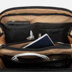 Close-up of opened SLNT E3 Faraday Crossbody Organizer Bag with items such as a camera, pens and passport tucked into the pockets inside but from the front 